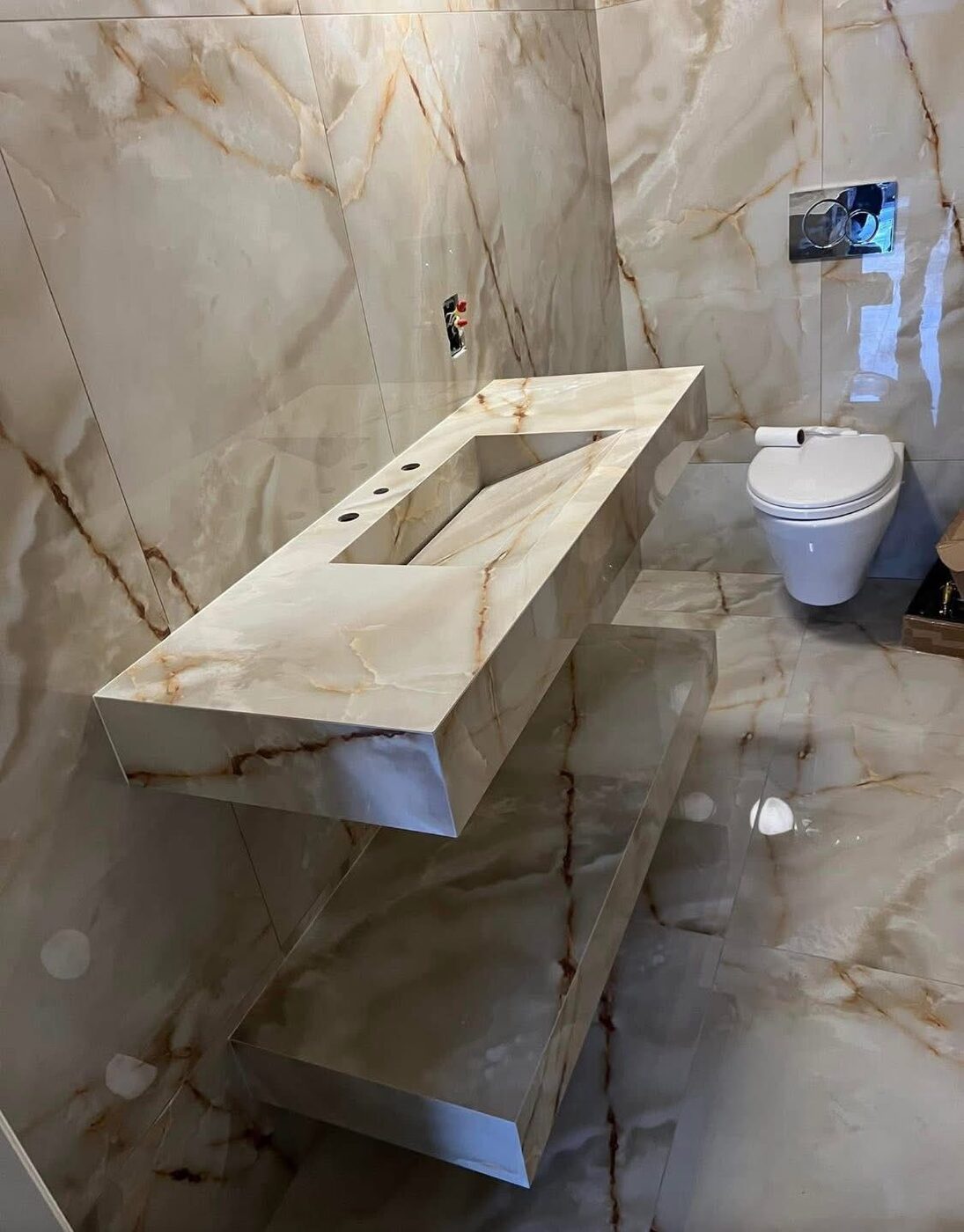 Floating stone vanity with a book-matched slab wall by Island Granite